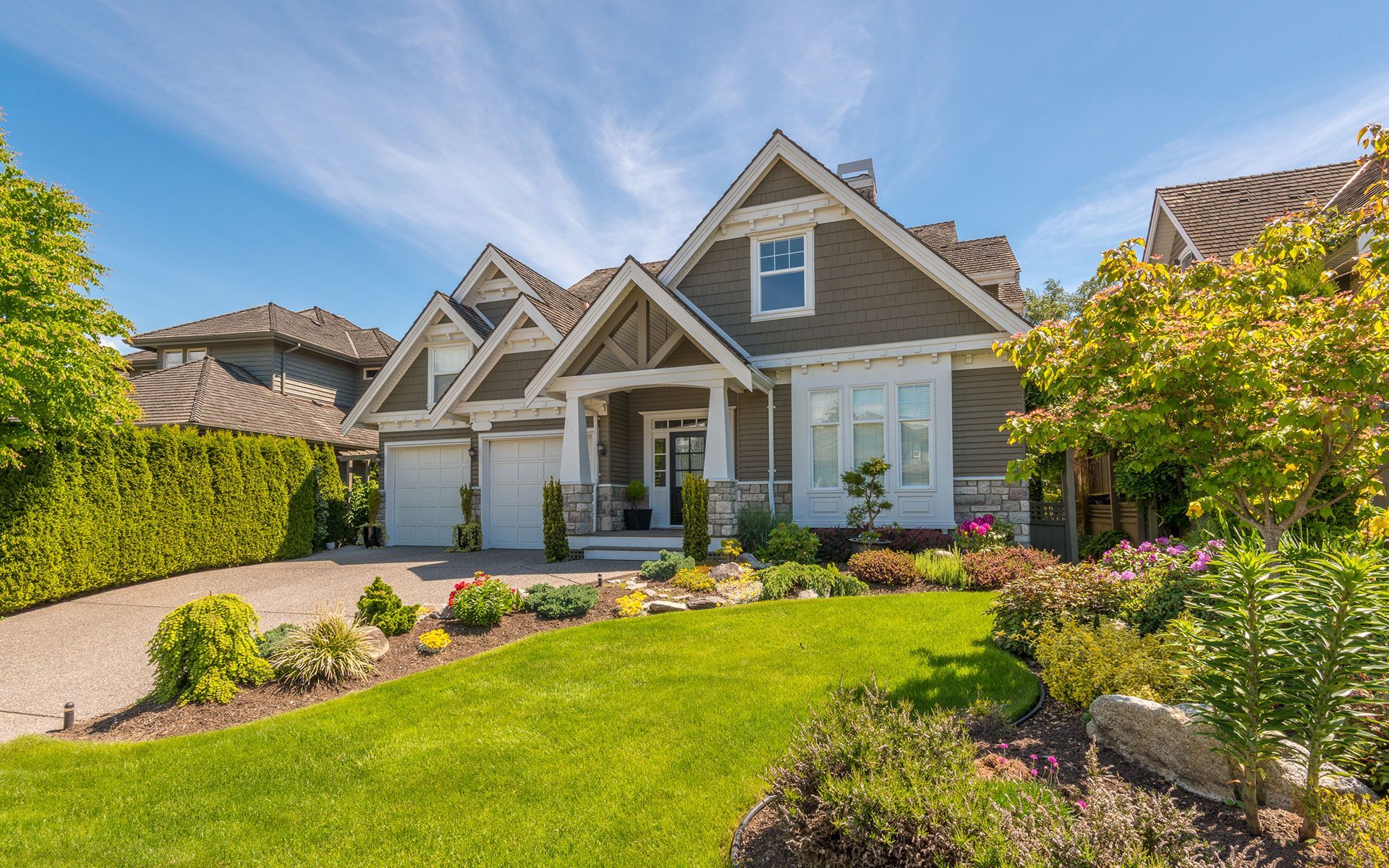 House with a well-kept green lawn, garden, and driveway on a sunny day.