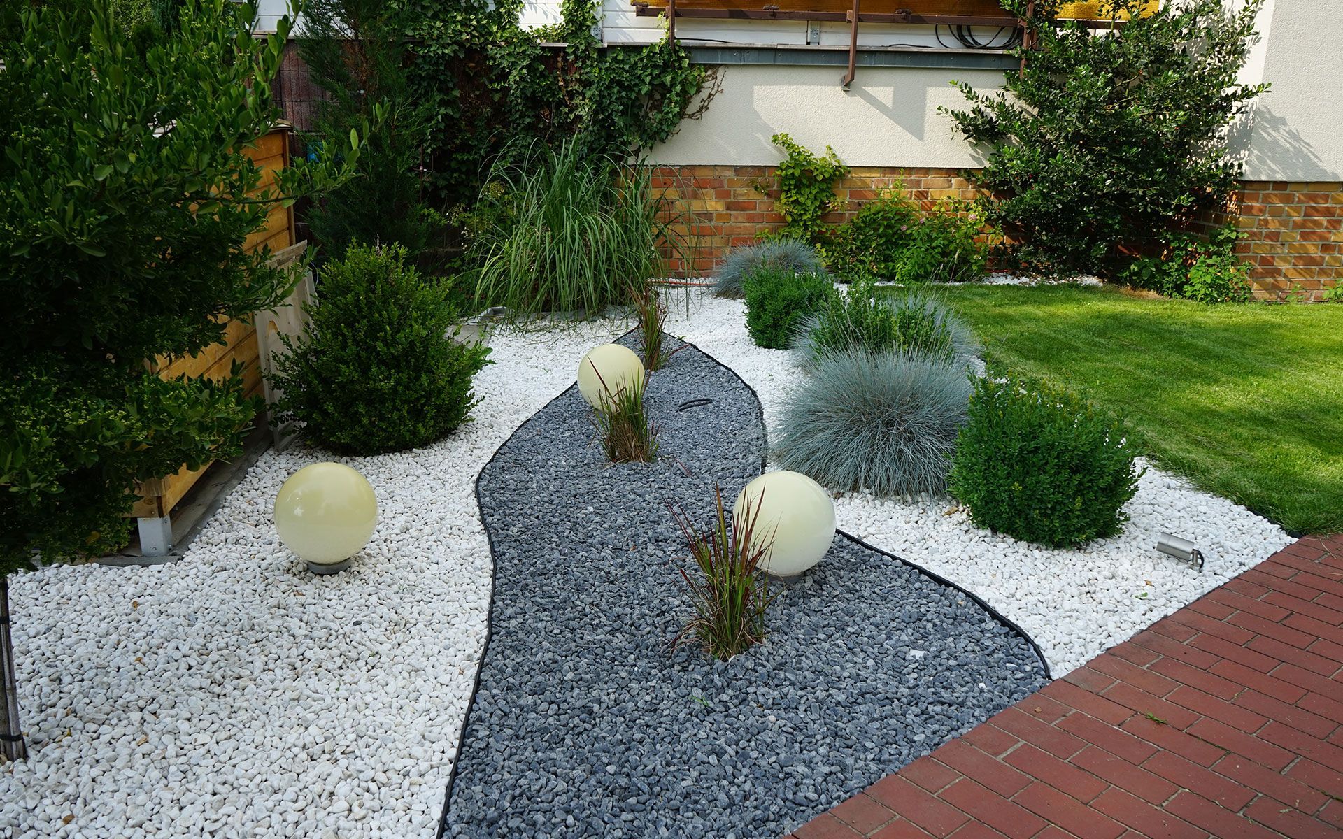 Garden bed with a gray gravel path, white gravel, spherical lights, and various green bushes.
