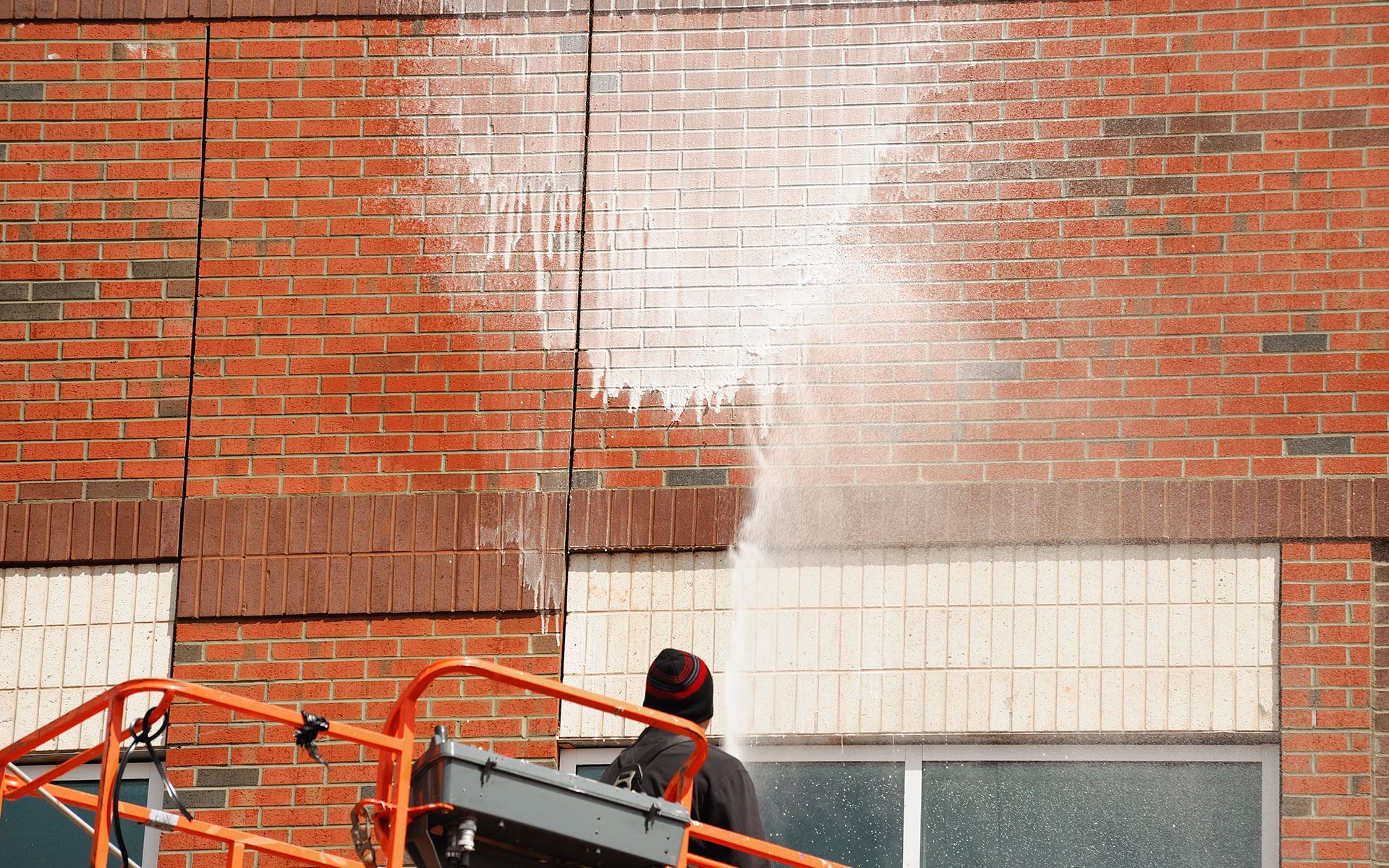 Person on lift spraying white substance onto brick building wall.