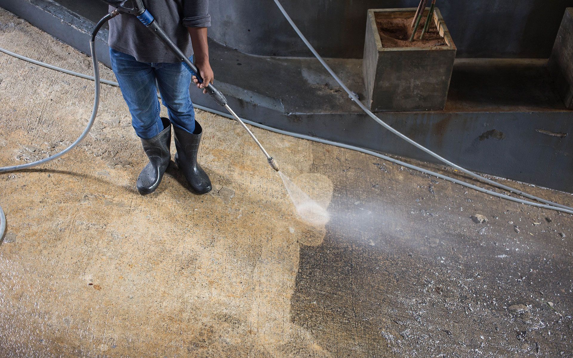 Person pressure washing a concrete surface outdoors.