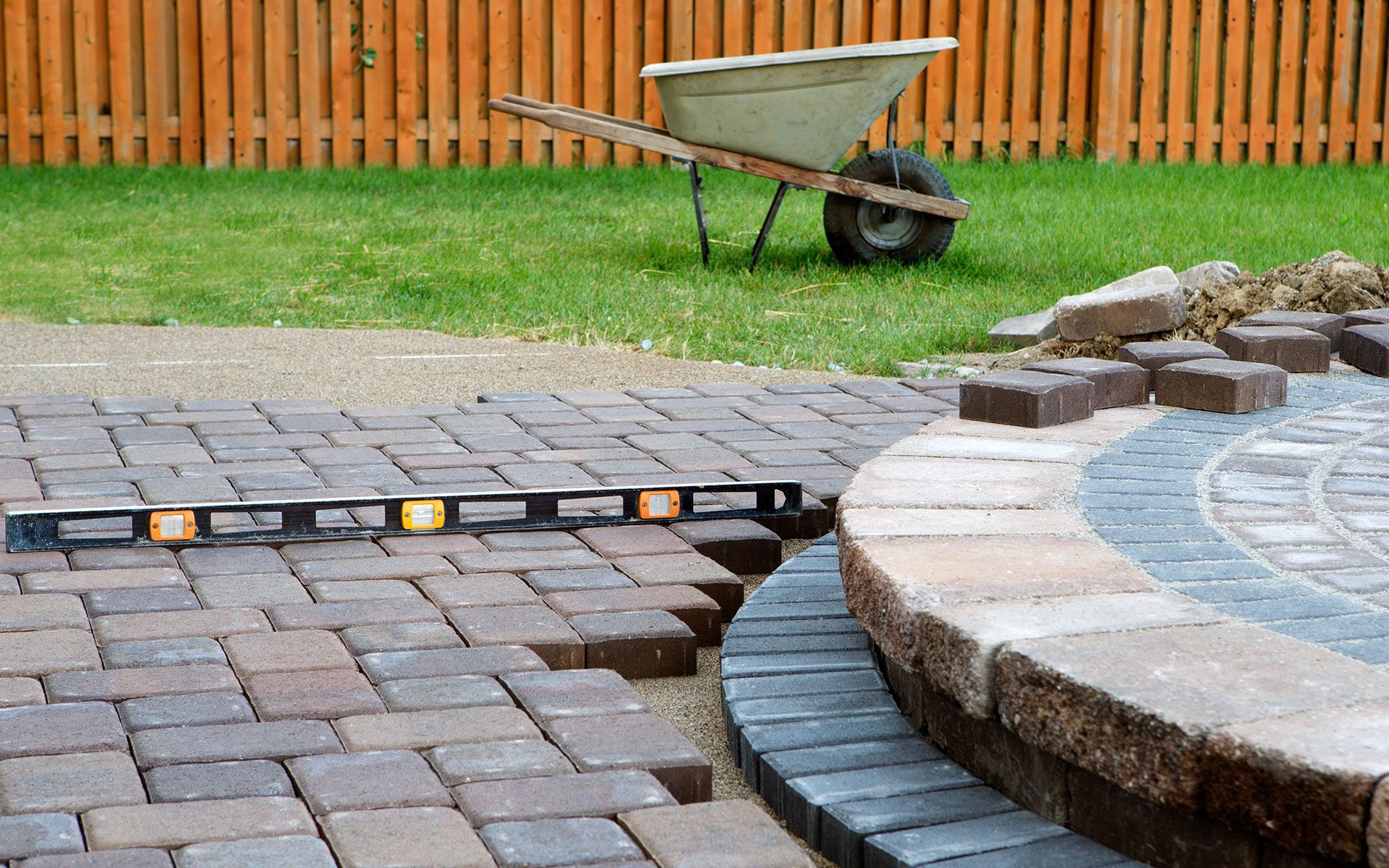 Brick patio being built with wheelbarrow and level in a backyard.
