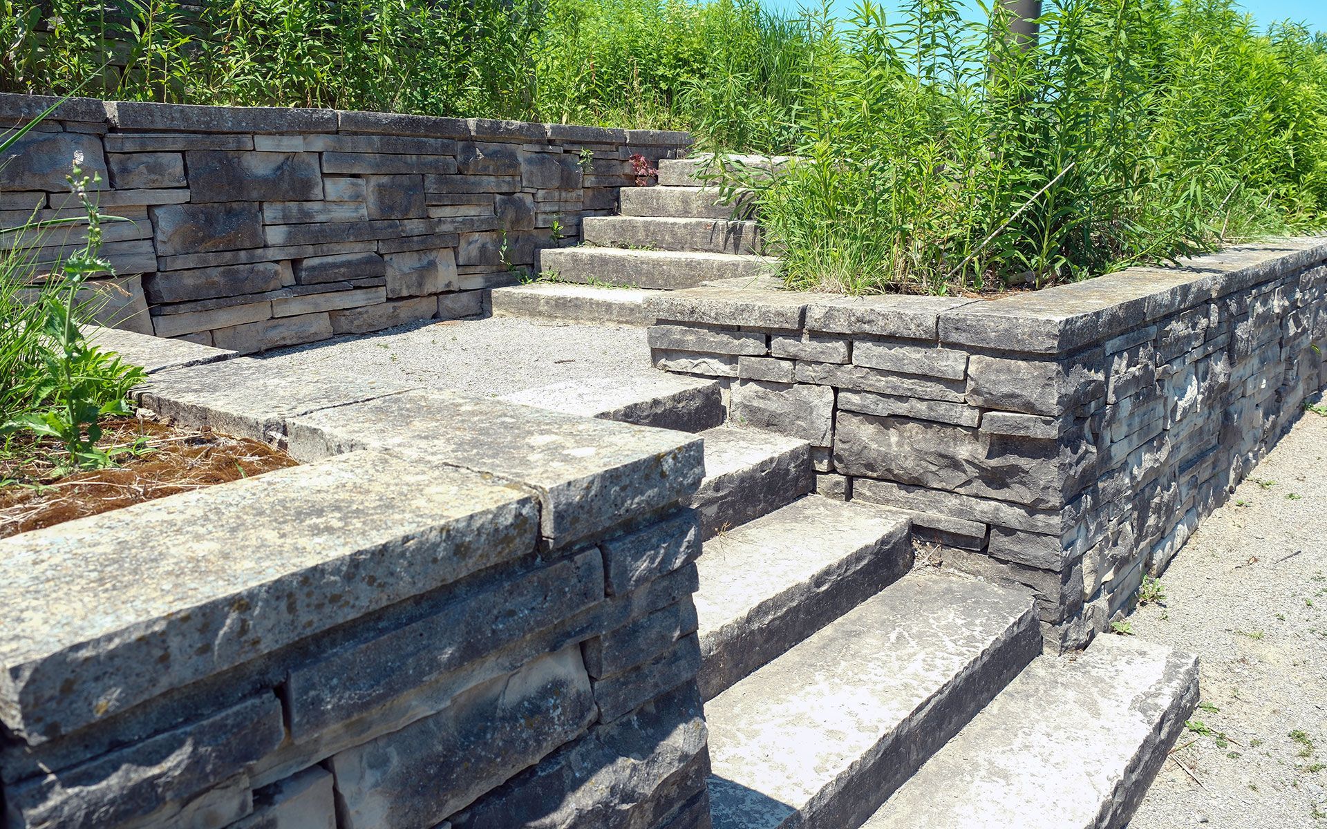 Stone steps and retaining walls in a garden setting, with gravel path and greenery.