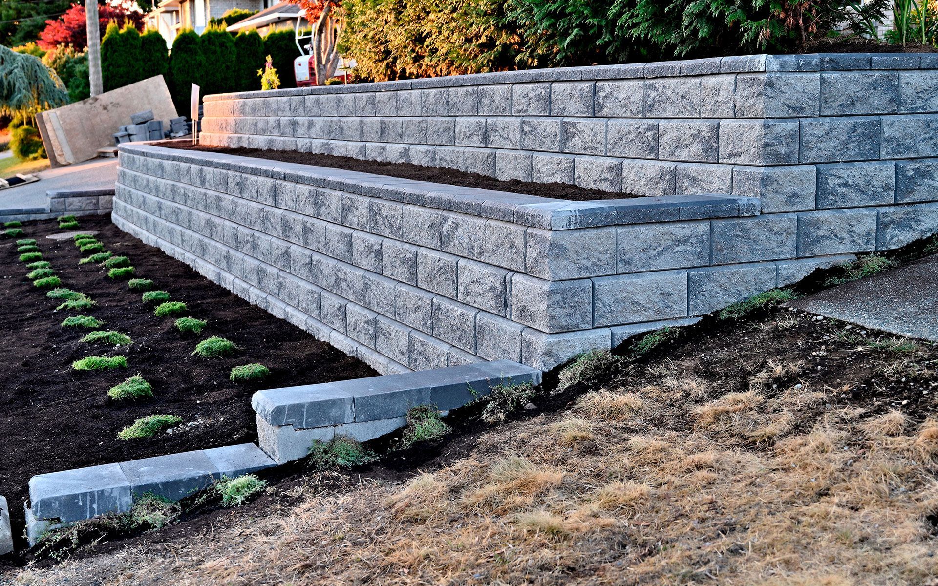 Retaining wall made of gray stone blocks, tiered, with planted garden in front.