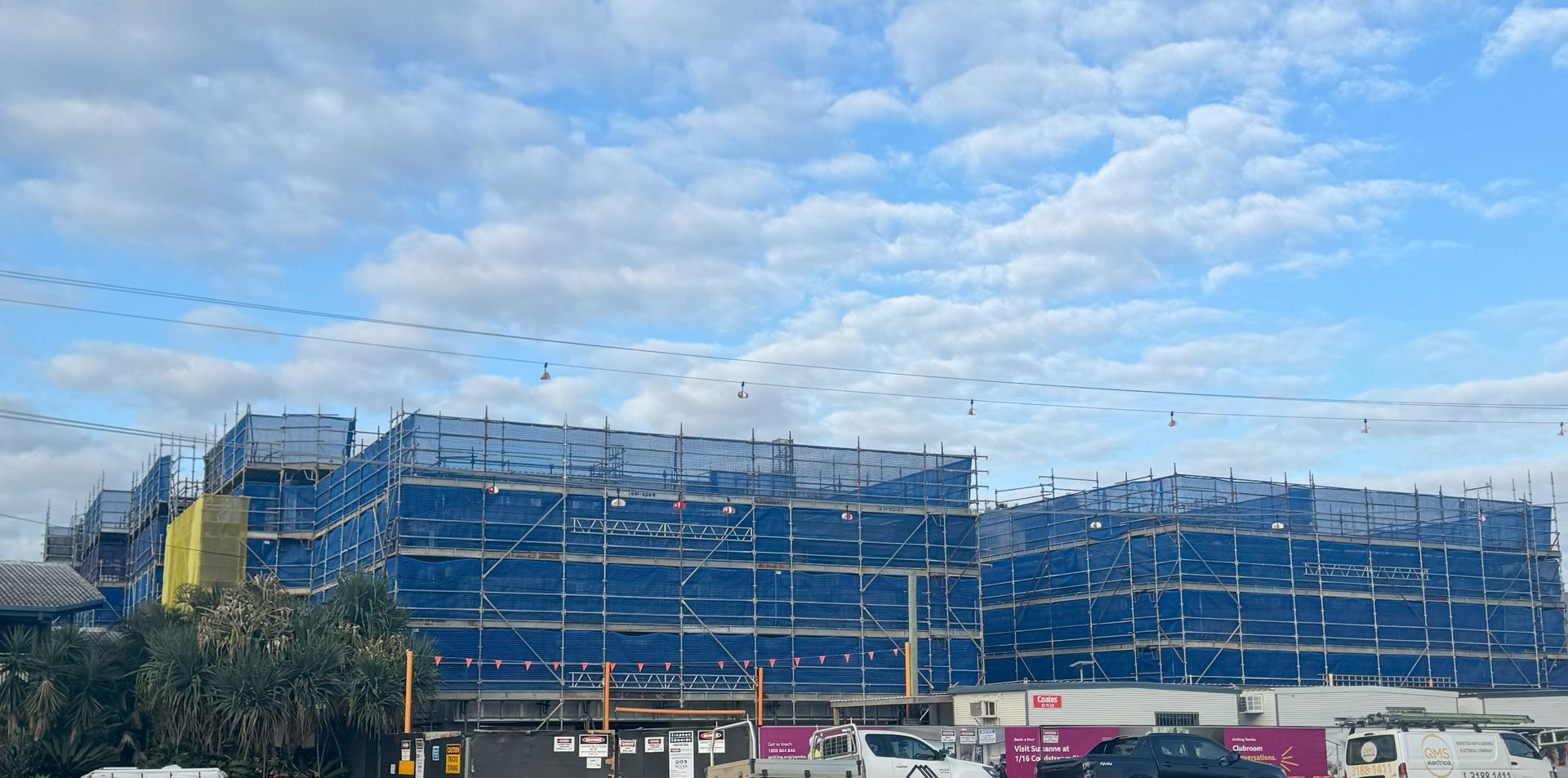 Building Under Construction With Blue Scaffolding Against A Cloudy Sky — Big River Scaffolding Solutions Pty Ltd in Coffs Harbour, NSW