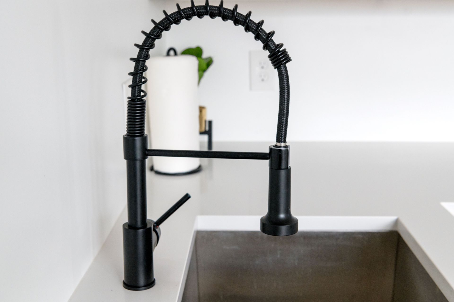 Black kitchen faucet over a stainless steel sink with a white paper towel roll in the background