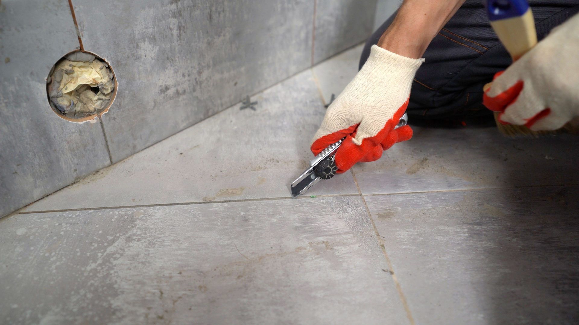 Worker sealing a concrete wall corner with a caulking gun, wearing gloves and a red sleeve
