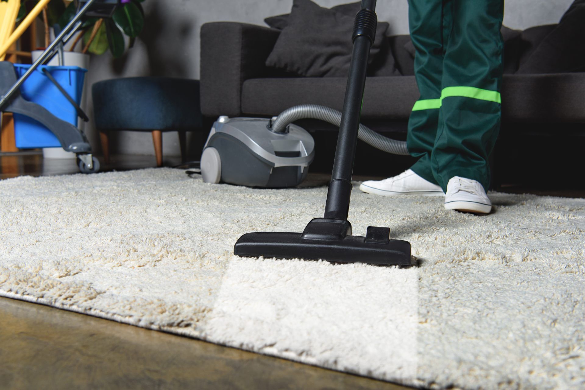 Person vacuuming a white rug in a living room with a black couch and a backpack nearby