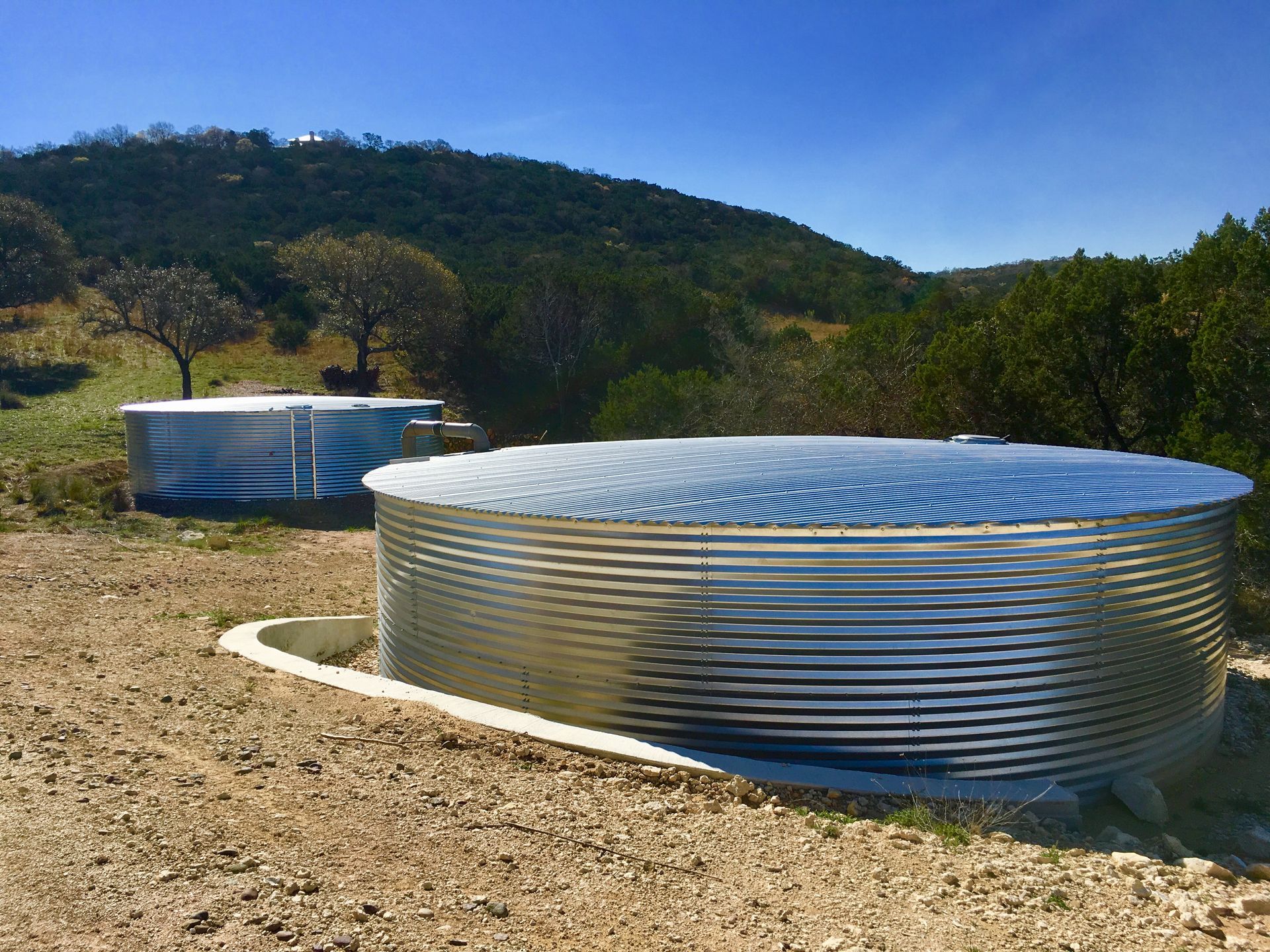 Two metal water tanks are sitting on top of a dirt field.
