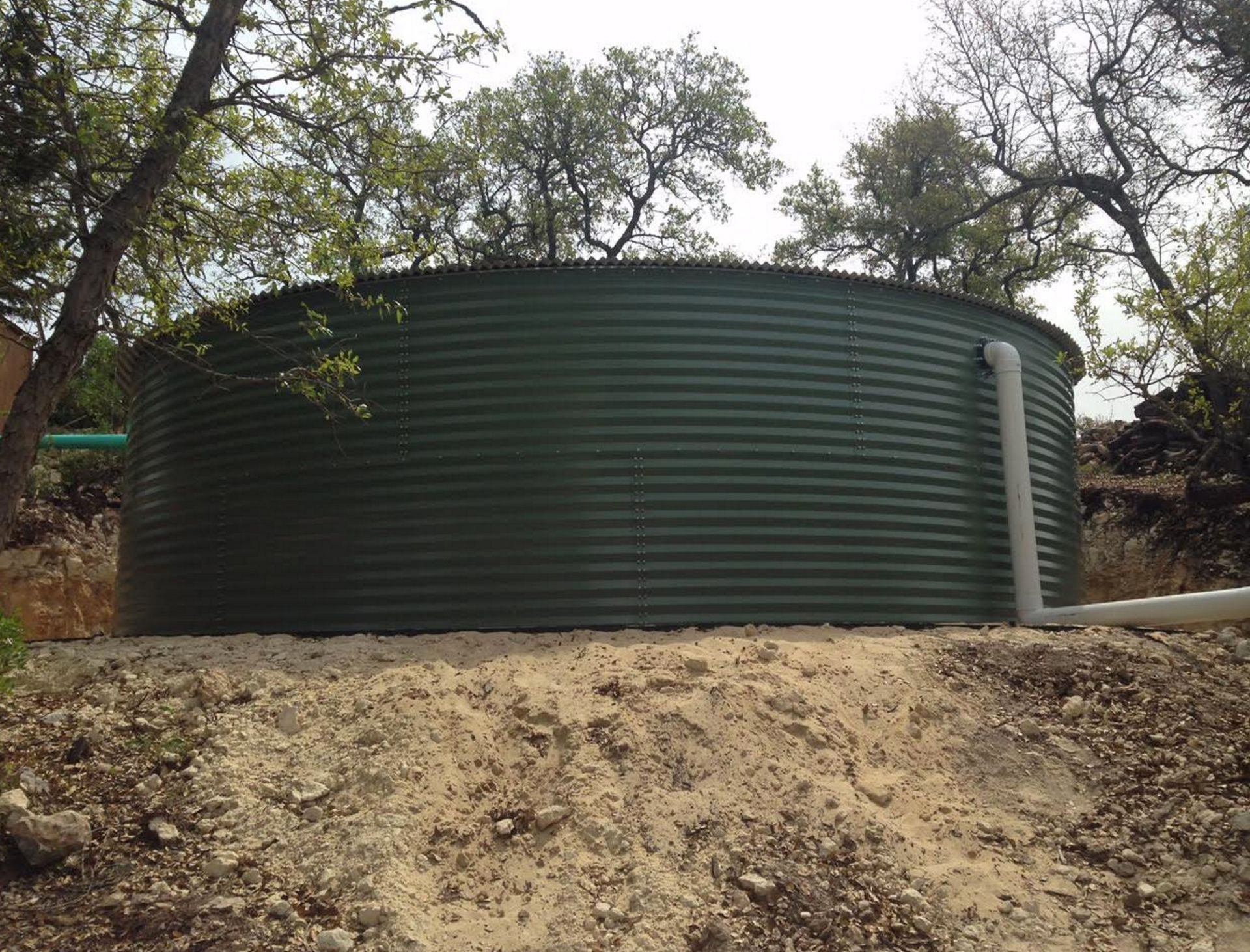 A large green water tank is sitting on top of a dirt hill.