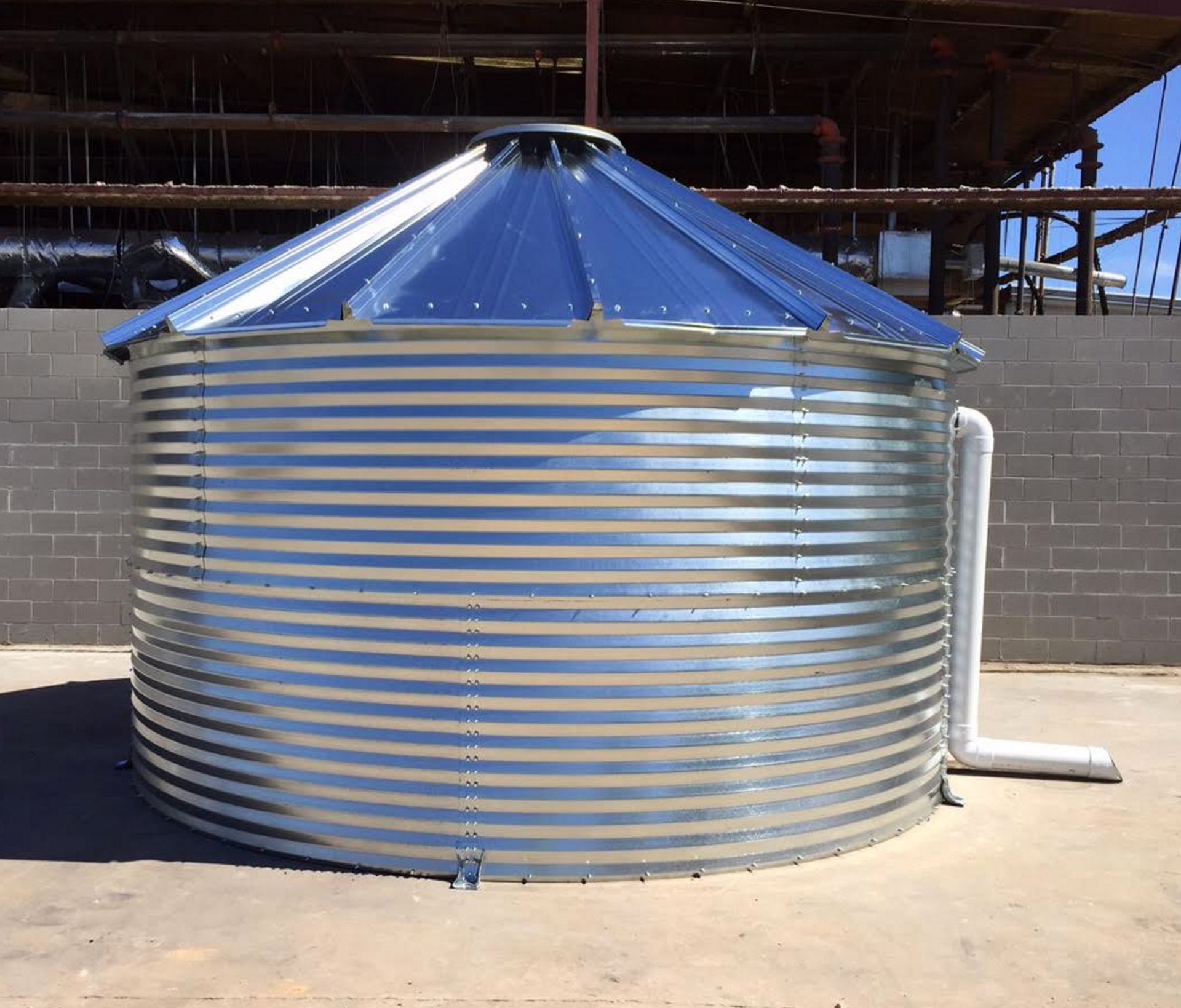 A large metal silo with a blue roof and a pipe attached to it