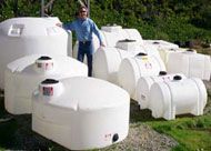 A man is standing in front of a row of white plastic tanks.