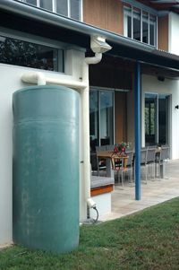 A large green water tank is sitting in front of a house.