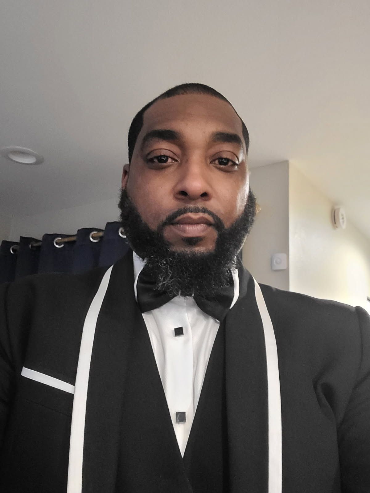 A man with a beard is wearing a tuxedo and bow tie.