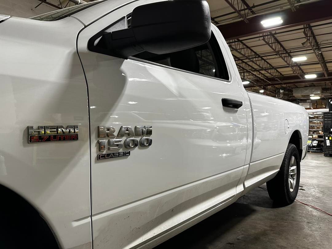 White Dodge Ram 1500 truck parked indoors. Side view showing HEMI emblem and black door handle.