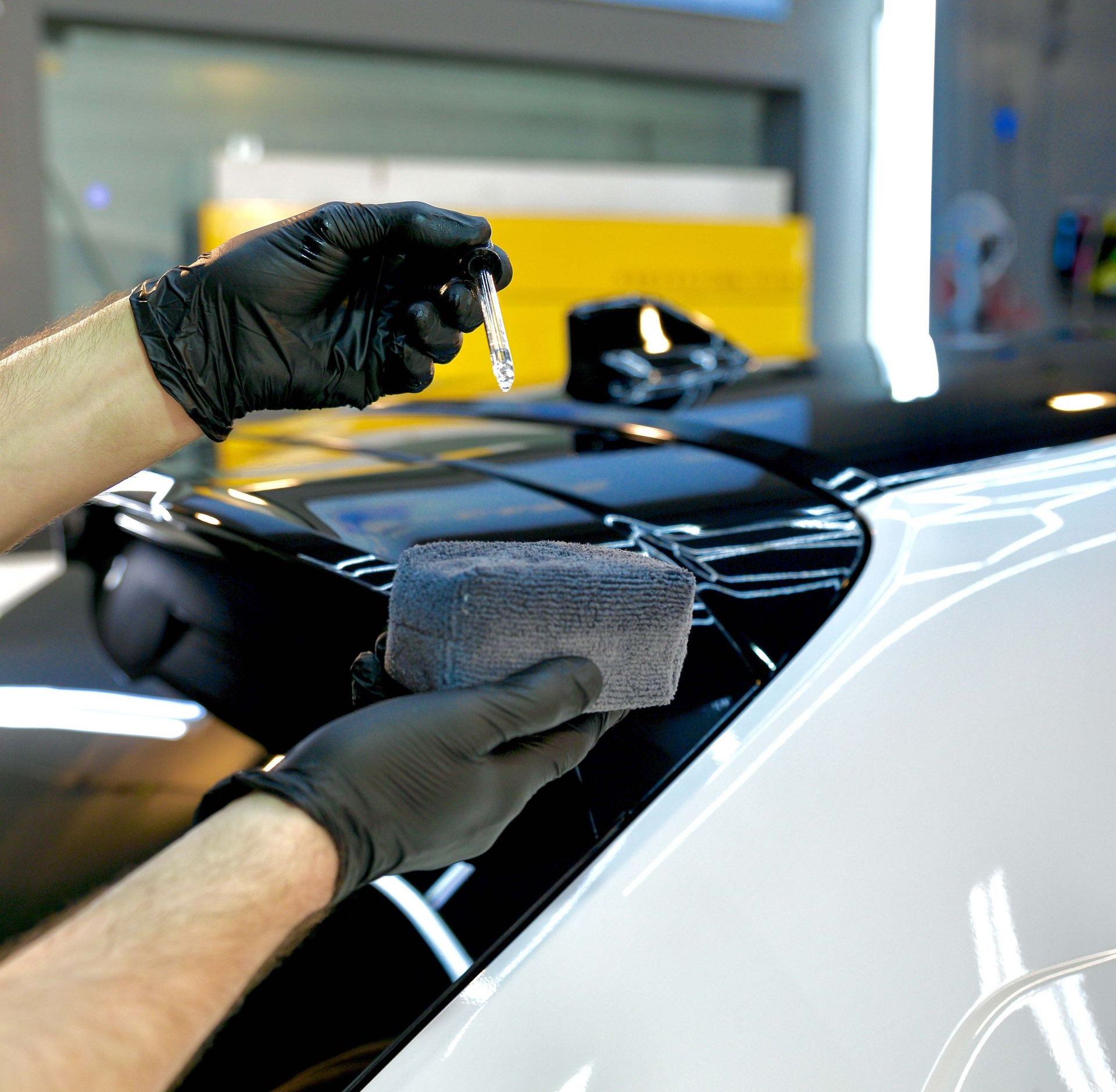 Hands in black gloves applying ceramic coating to a car's black and white paint.