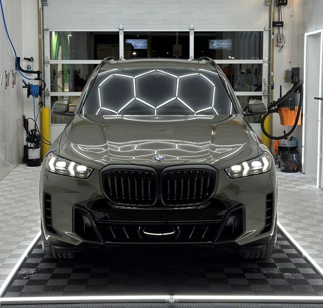 Gray BMW SUV parked inside a garage, under honeycomb-shaped lights.