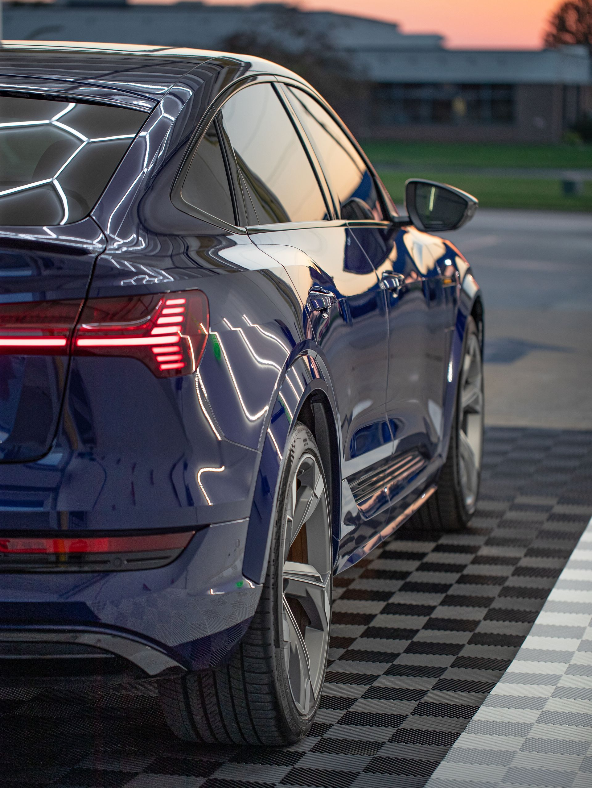 Dark blue Audi e-tron SUV from the rear, parked on a checkered floor with a sunset in the background.
