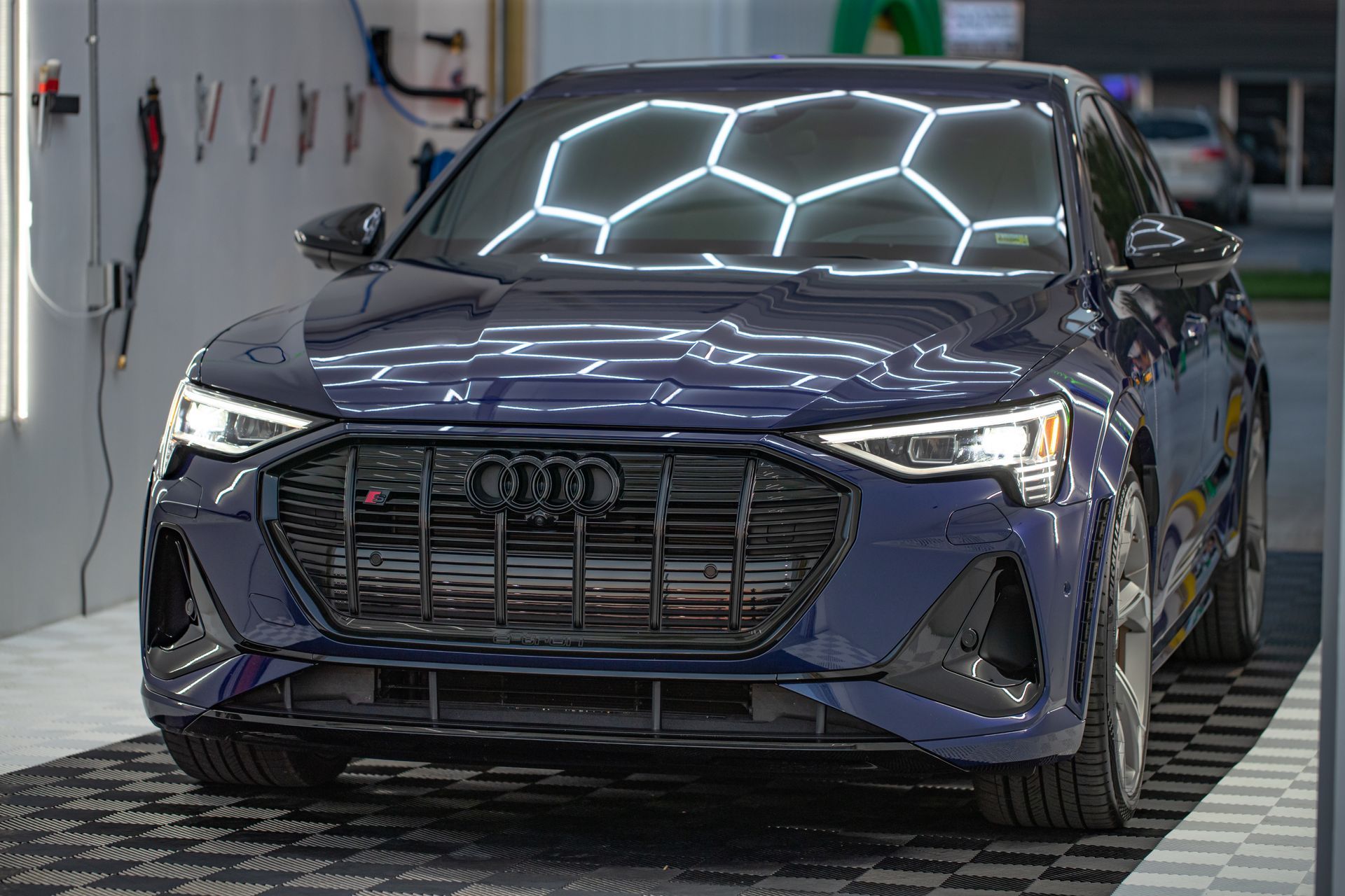 Dark blue Audi car in a well-lit garage, front view. Black grill, honeycomb lighting.