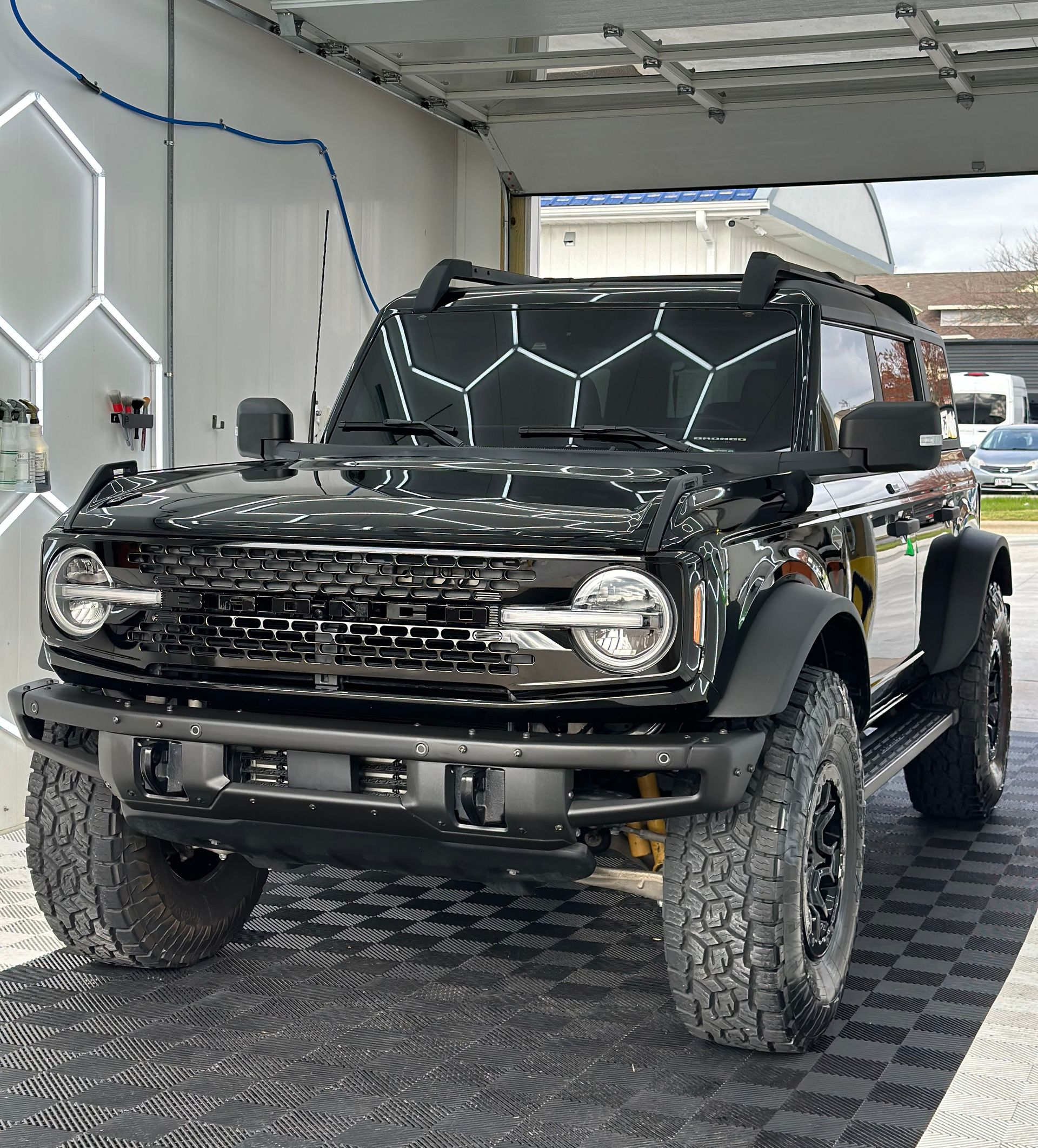 Black Ford Bronco SUV parked in a car wash bay under hexagonal lights.