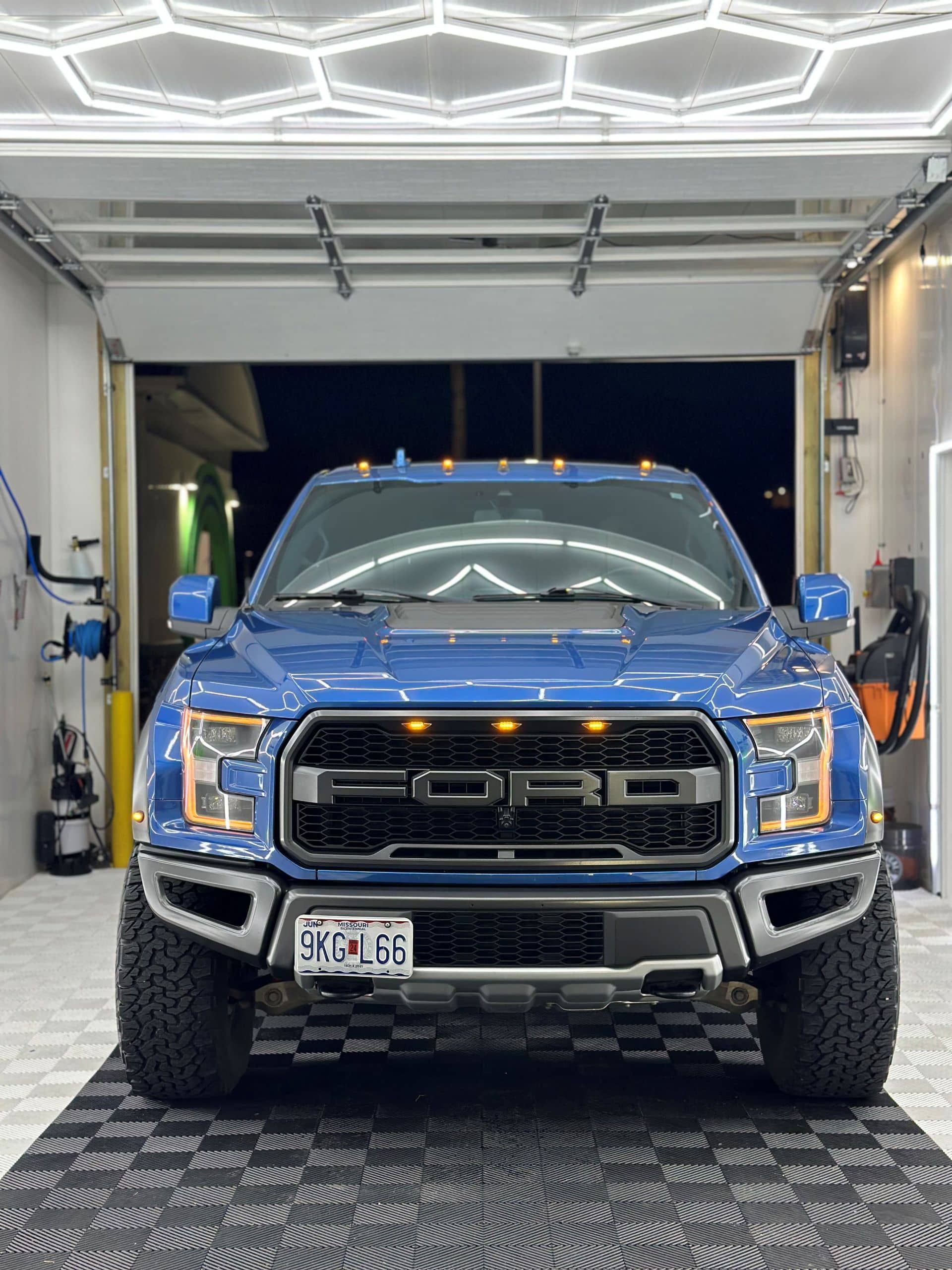 Blue Ford Raptor truck parked in a garage with overhead lights.