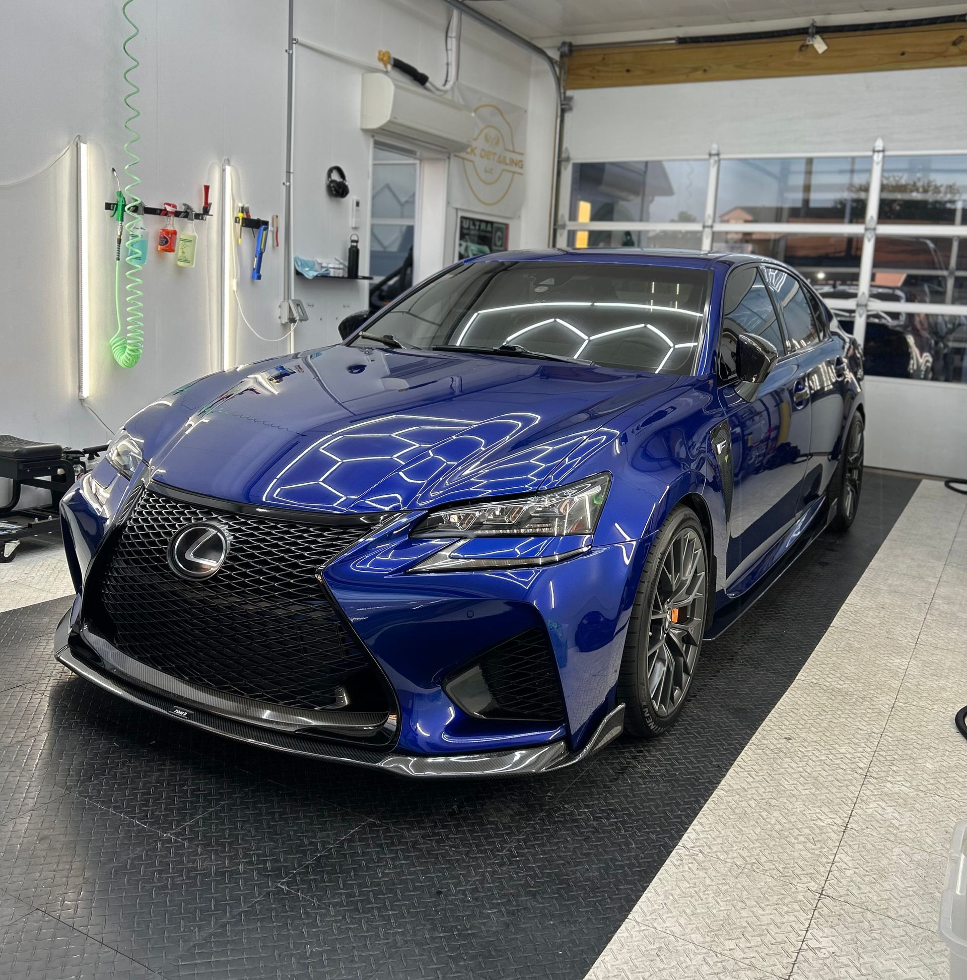 Blue Lexus sports car in a garage with black and gray tiled floor, under hexagonal lights.