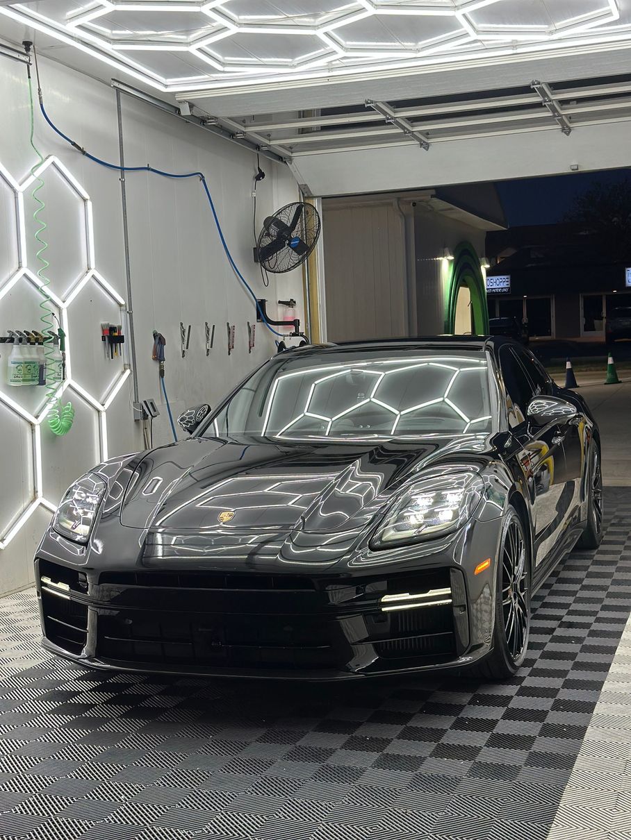 Two men stand next to a blue Ford truck in a brightly lit car wash bay.