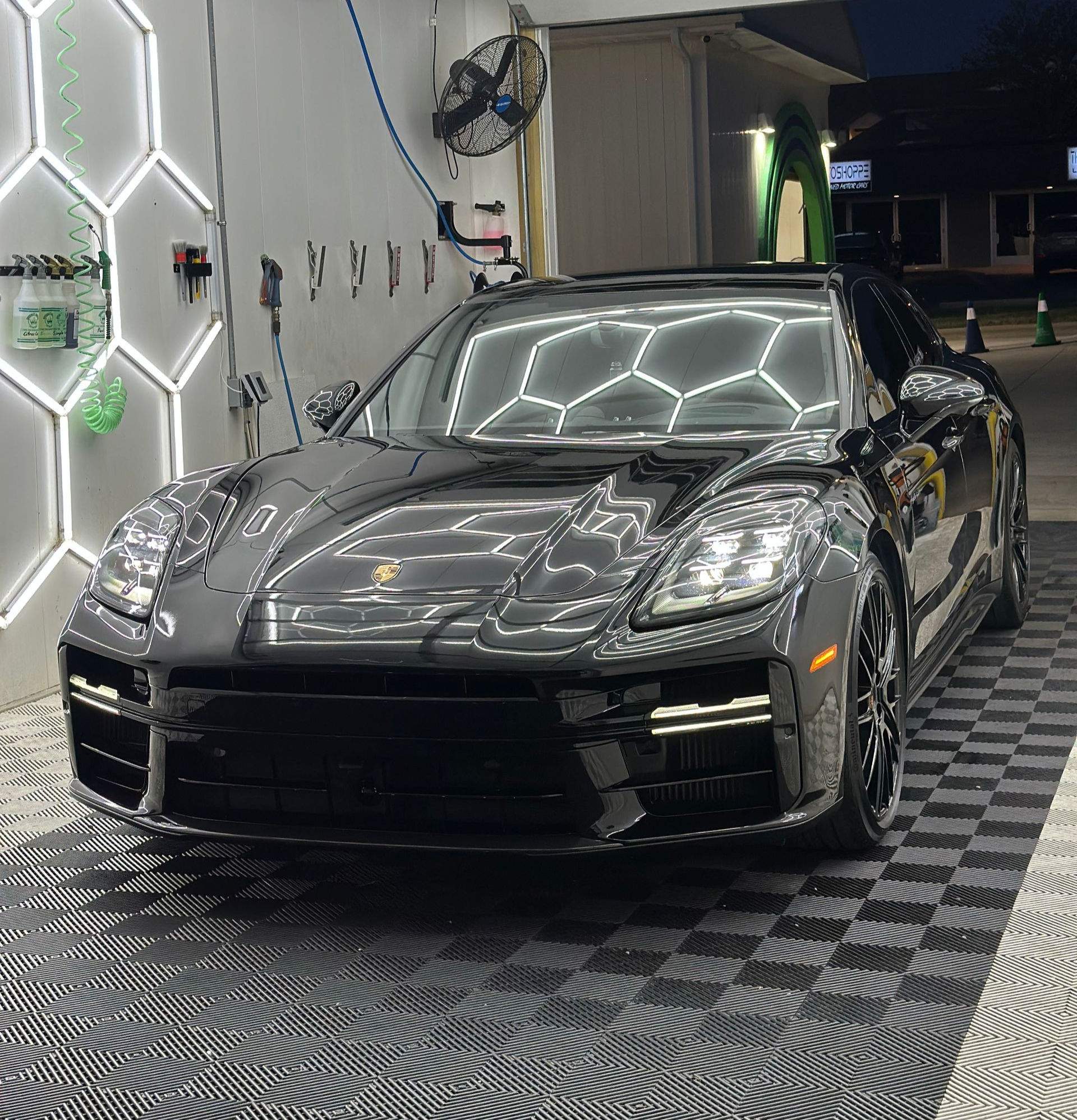 Black Porsche Panamera, freshly cleaned, parked in a car wash bay with hexagon lights.