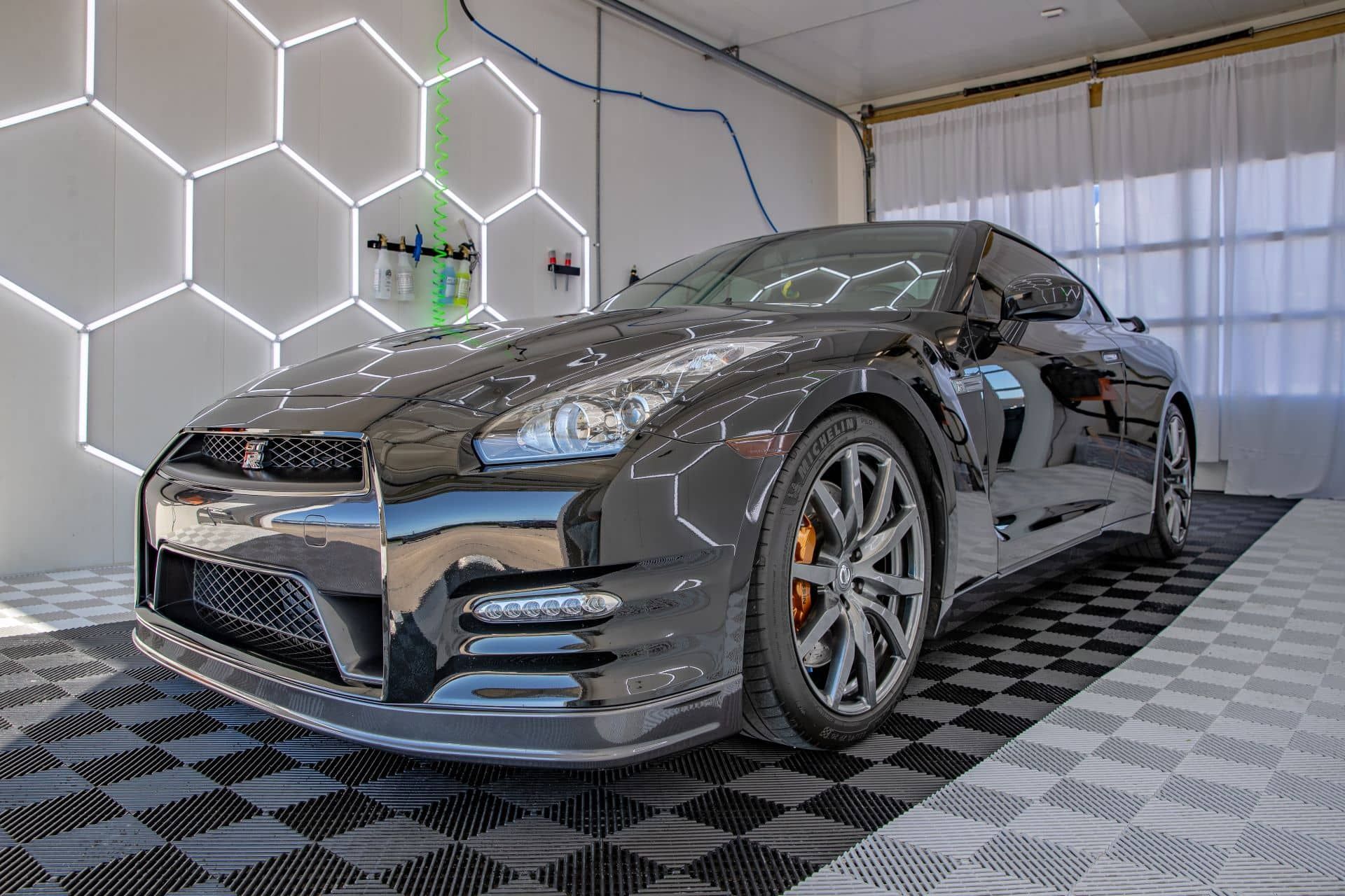 Glossy black Nissan GT-R sports car in a garage with honeycomb-shaped lights and tiled floor.