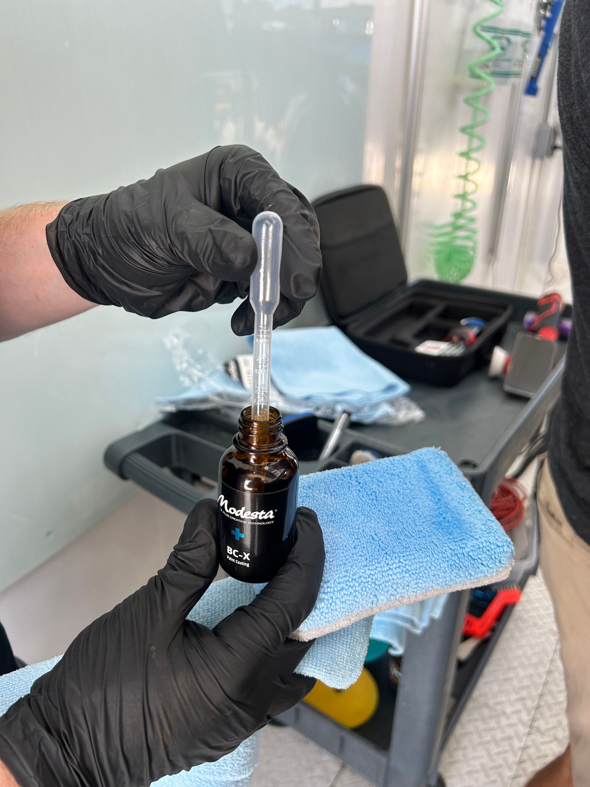 Modesta BC-05 glass coating product with a sample of glass coating held by tweezers on a reflective surface.