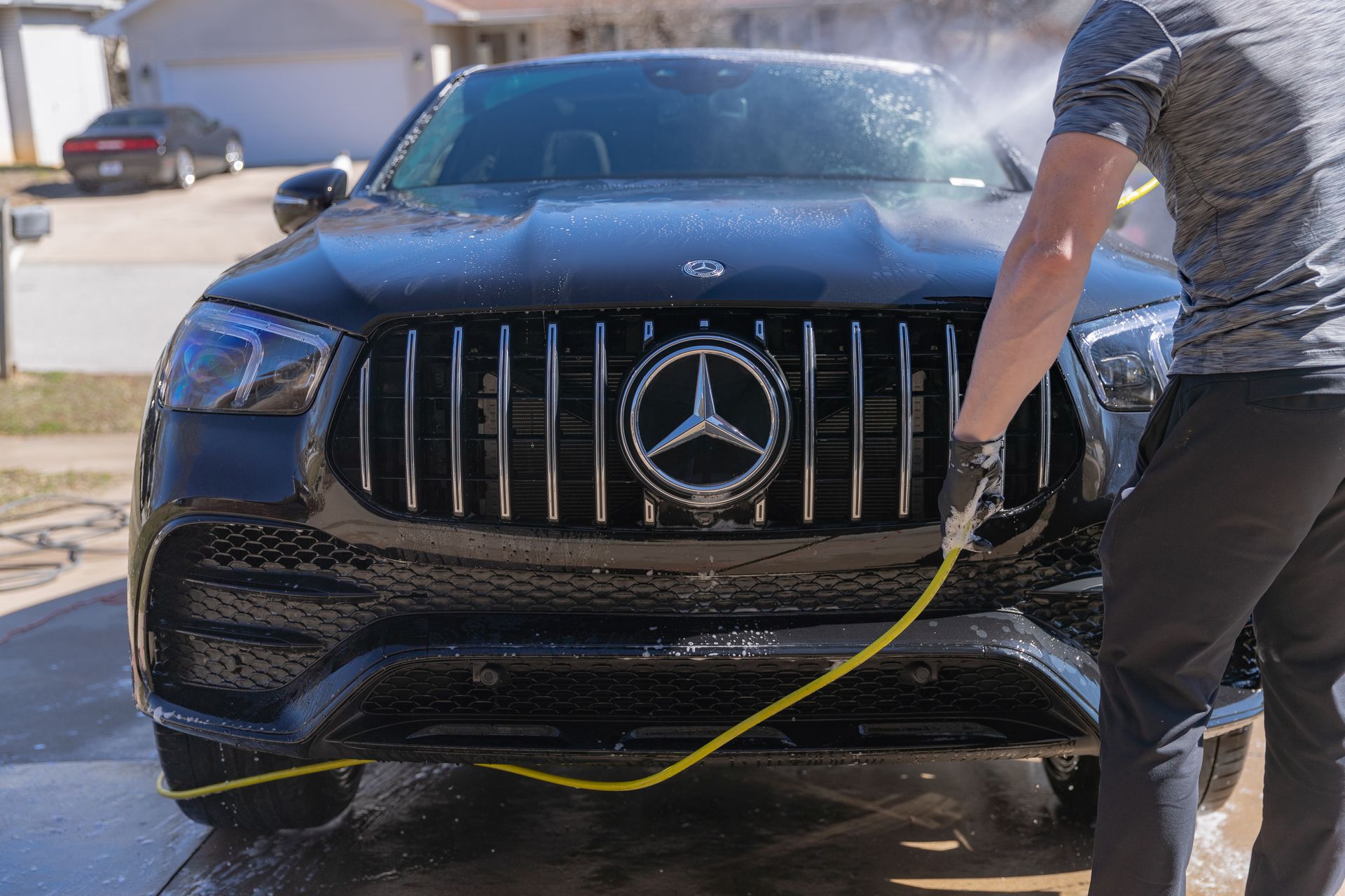 Person washing a black Mercedes SUV with a hose; outdoors.