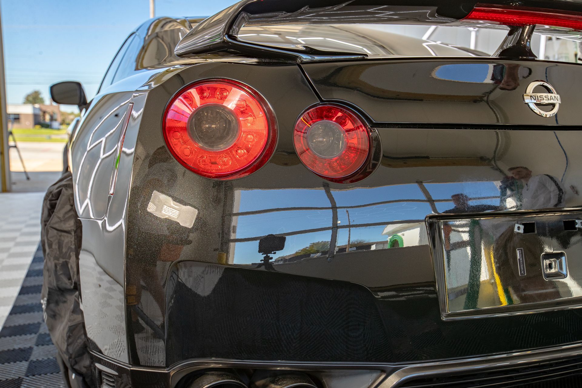 Black Nissan GT-R sports car rear with bright red taillights reflecting a clear, sunny sky.