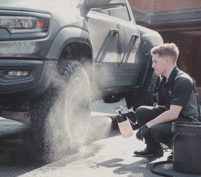 Two people washing a white Mercedes-Benz SUV in front of a brick building.