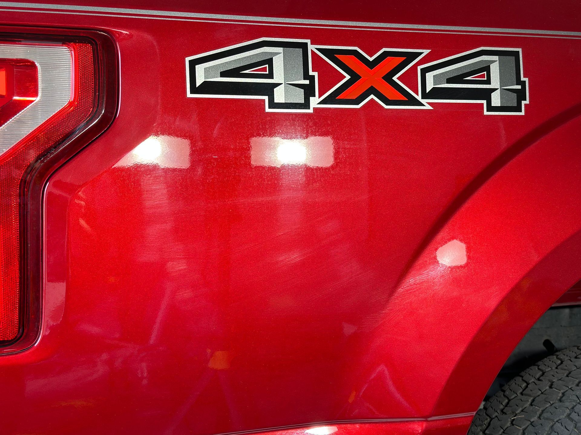 Red truck's rear quarter panel with 4x4 emblem, showing paint imperfections and a taillight.