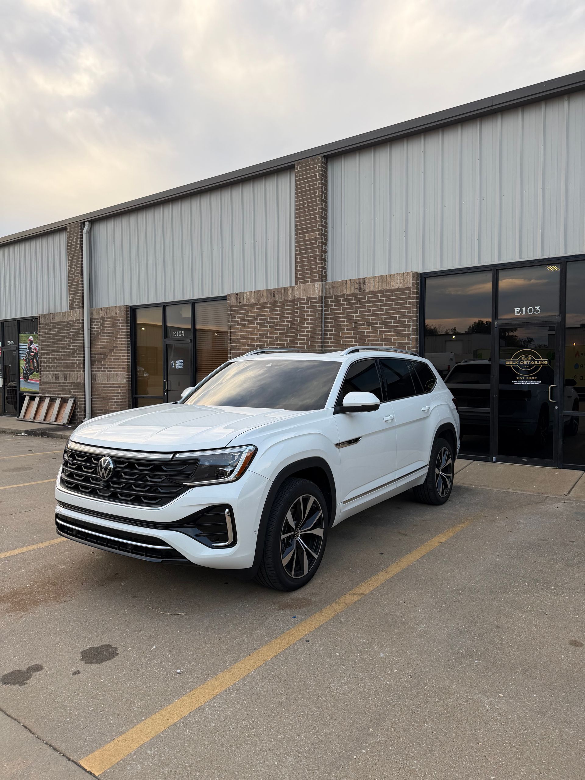 White Volkswagen Atlas SUV parked in front of a brick building with windows. Cloudy sky.