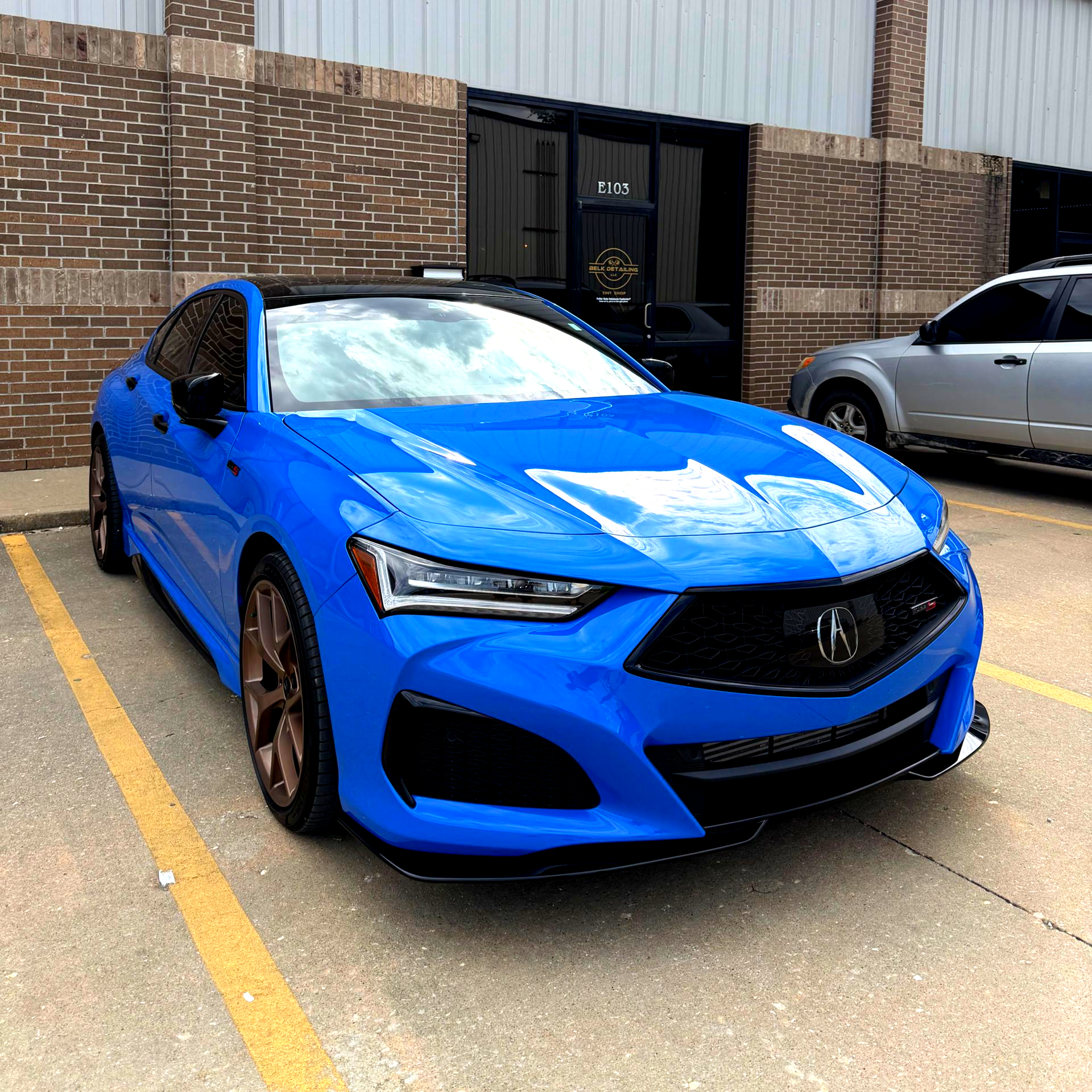 Blue Acura TLX sedan parked outside a brick building.
