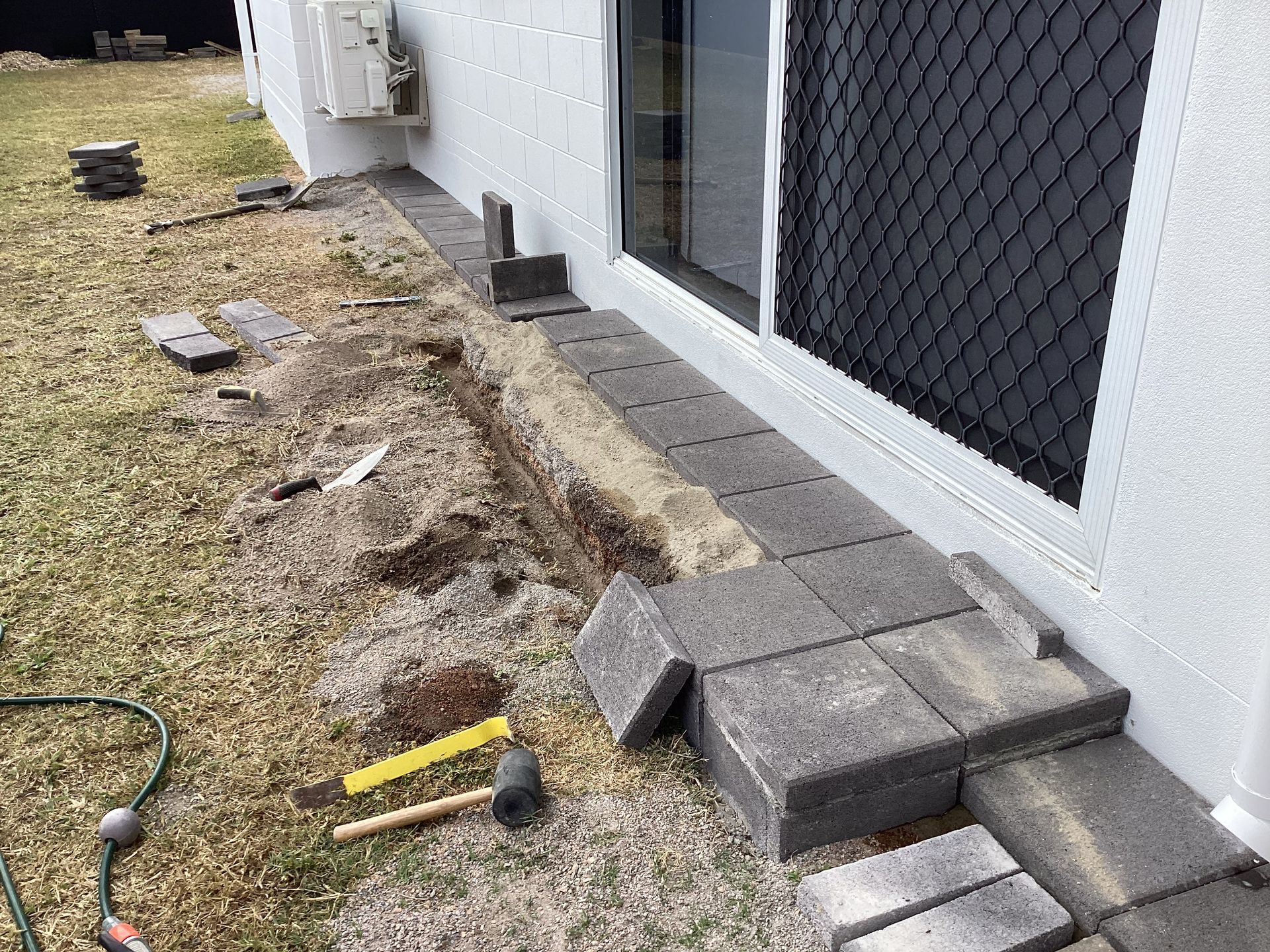 Damaged Ground and Loose Pavers Beside a White House Wall and Screened Door — My Handyman Townsville In Garbutt, QLD