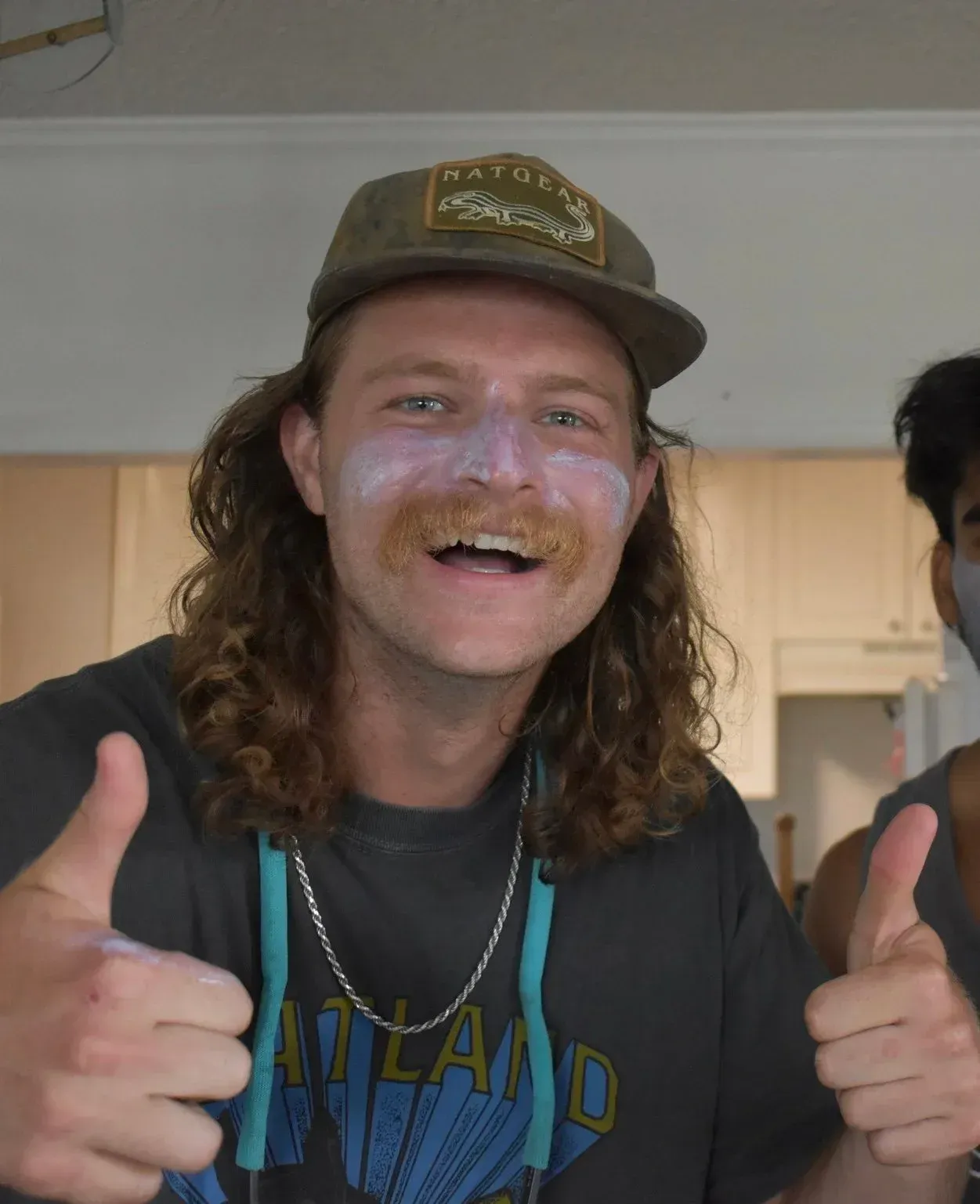 Man with sunscreen on his face, wearing a hat, giving a thumbs up.