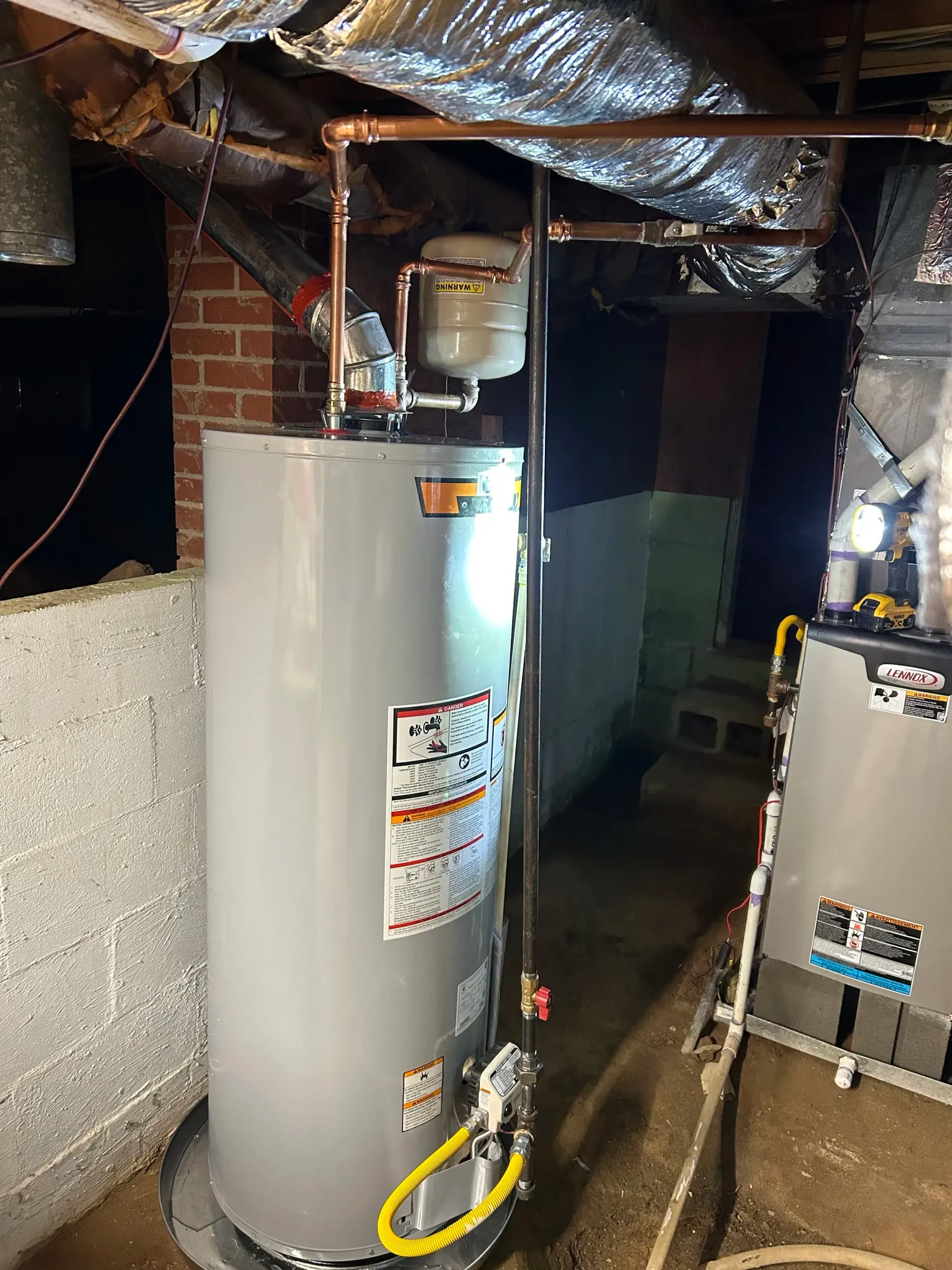 A gas water heater installed in a basement, with copper pipes and a gas line visible.