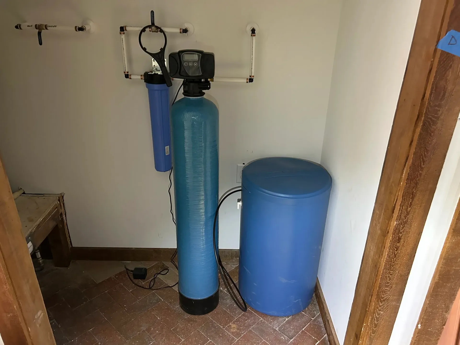 Water filtration system in a small white room, featuring blue tanks and pipes.