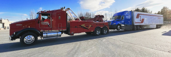 A red tow truck is towing a blue semi-truck | Collins Enterprises