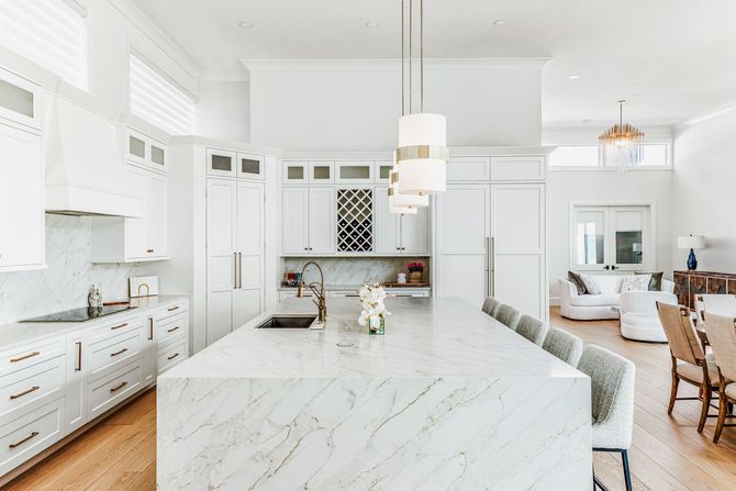 Spacious, bright white kitchen with large island, marble countertops, and pendant lights.
