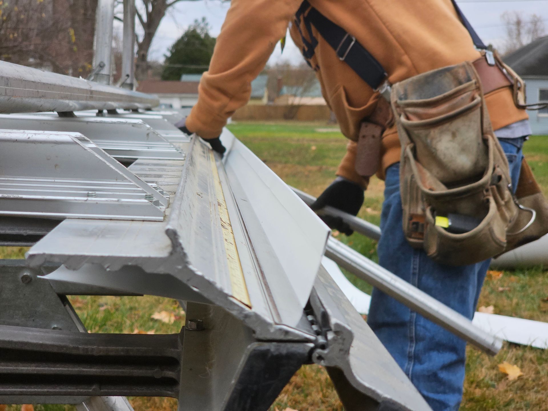 A man is standing on a ladder fixing a gutter on the roof of a house.