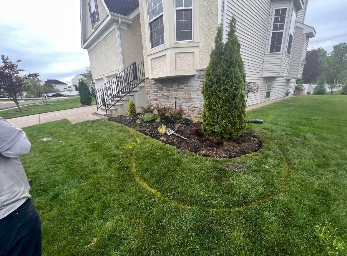 A person standing near a home with a curved flower bed full of mulch and plants.
