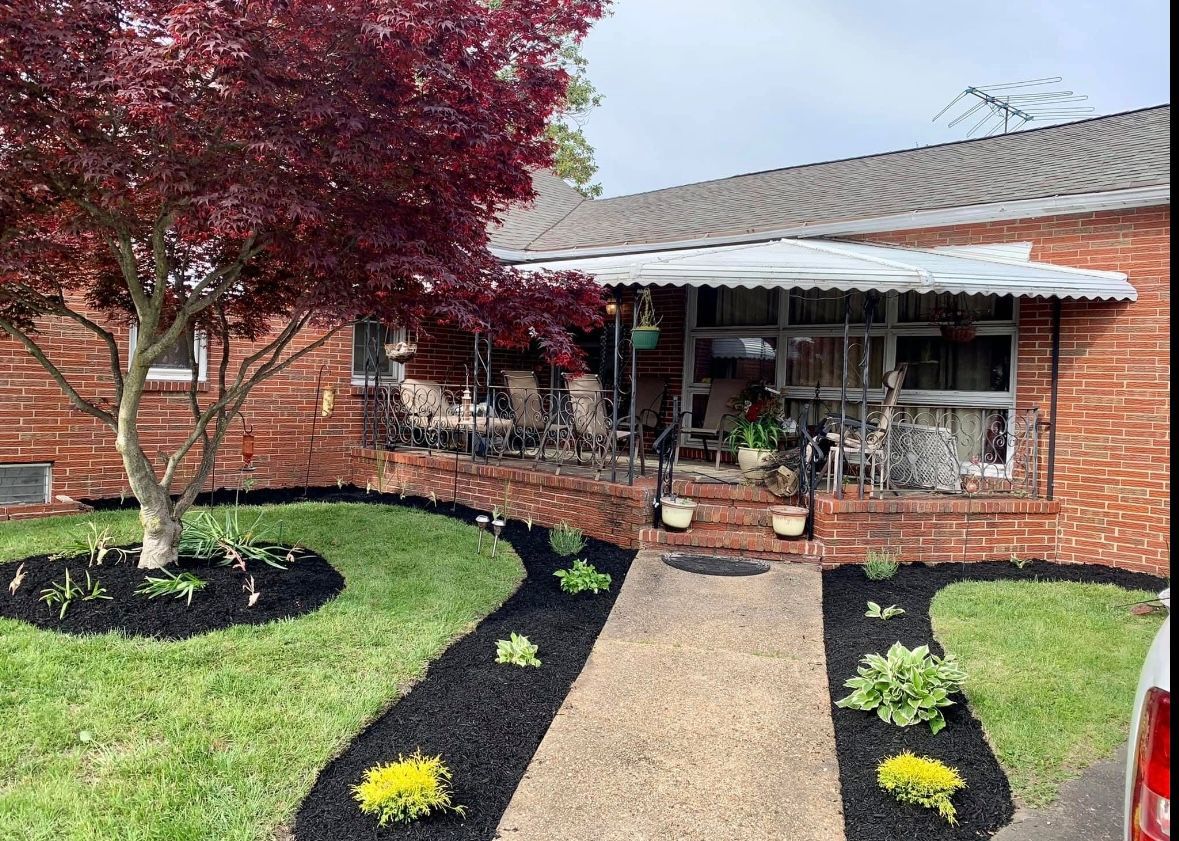 Brick house with a porch, red tree, walkway with plants, and black mulch.