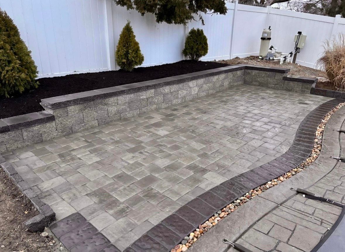 Stone patio surrounded by retaining walls, mulch, and a white fence.