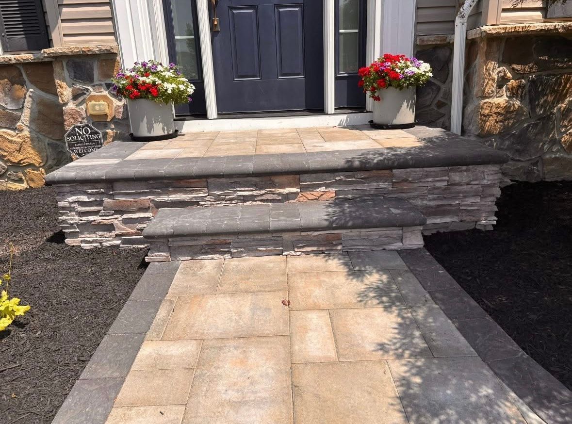A front porch with steps, stone facade, and flower pots. Pathway leads to a blue door.