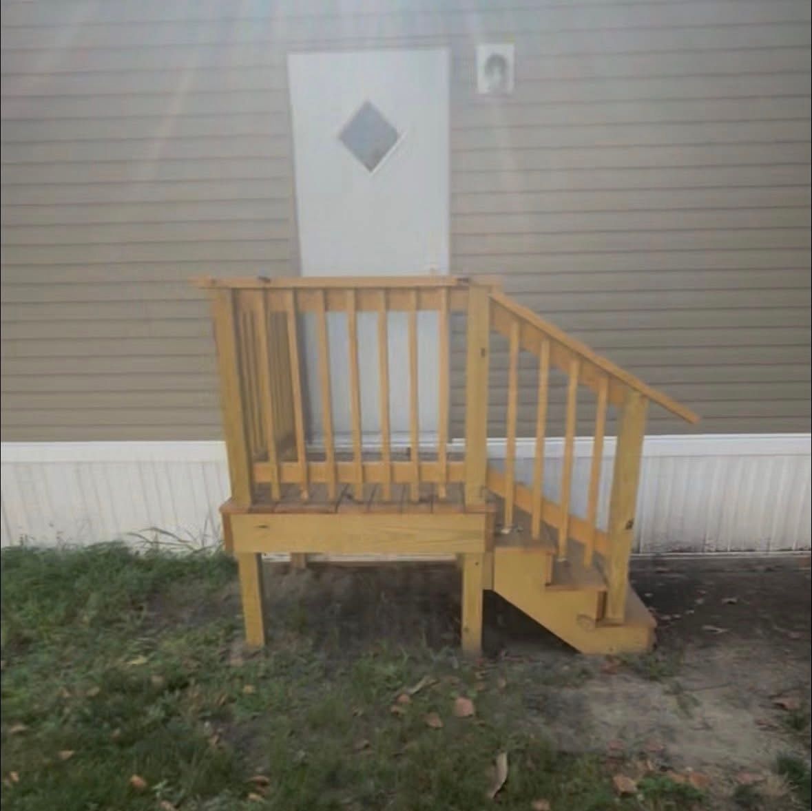 Wooden outdoor steps leading to a white door, with tan siding and grass surrounding.