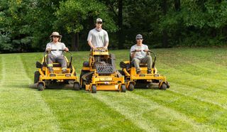 Three people on yellow riding lawnmowers mowing a green lawn. Three people on yellow riding lawnmowers mowing a green lawn.