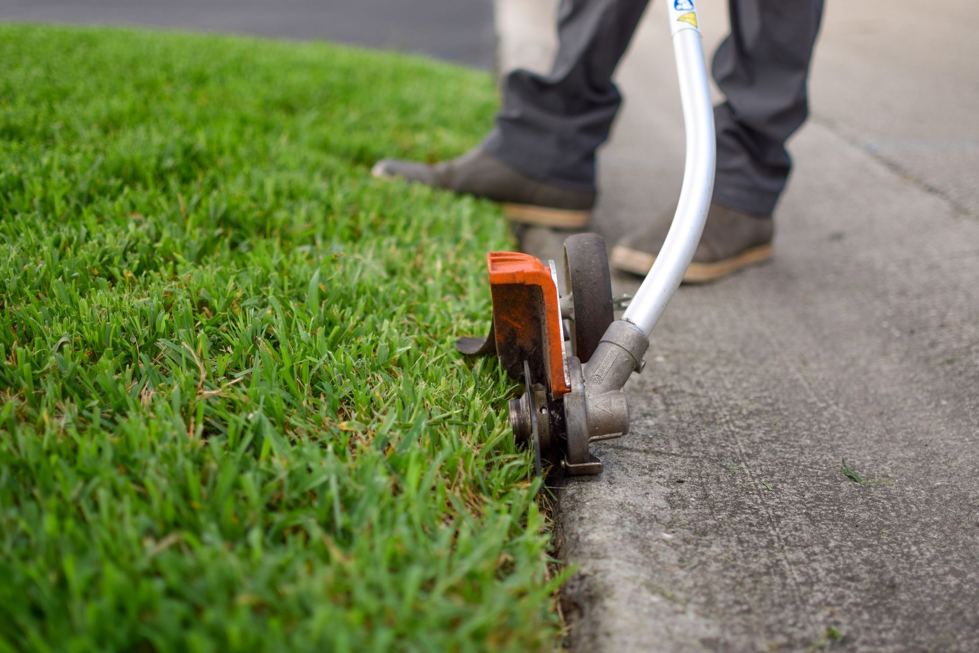 Person using a weed wacker to trim grass along a concrete curb.