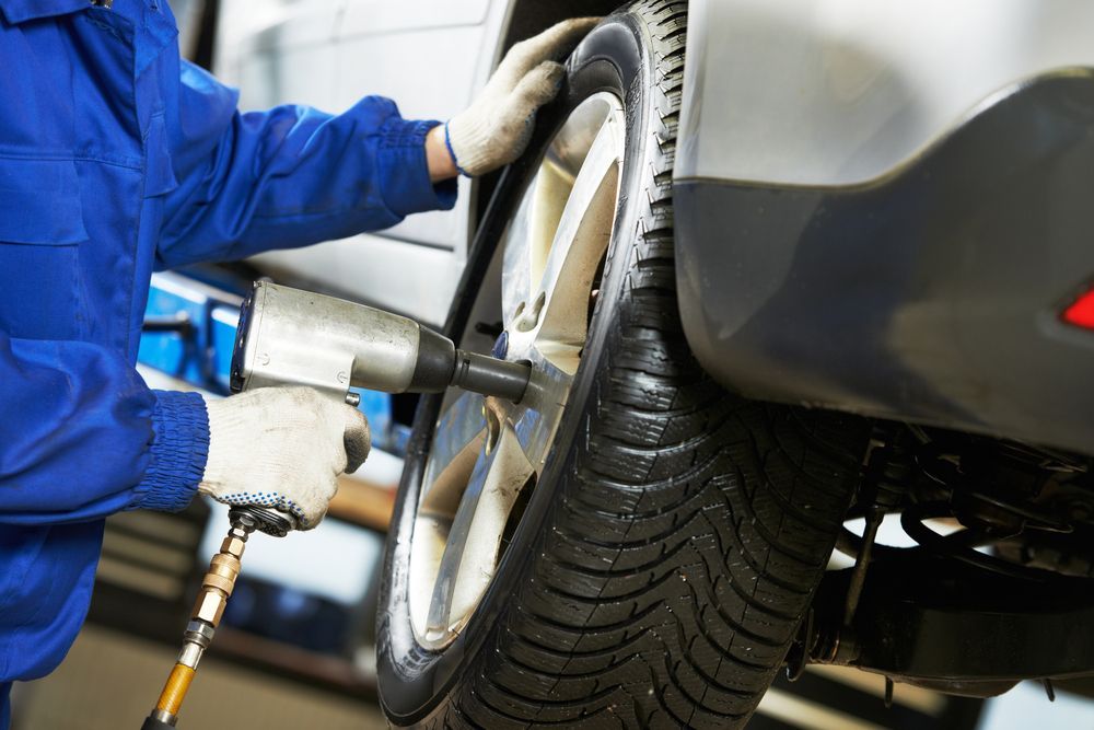 A man is changing a tire on a car with an air wrench.